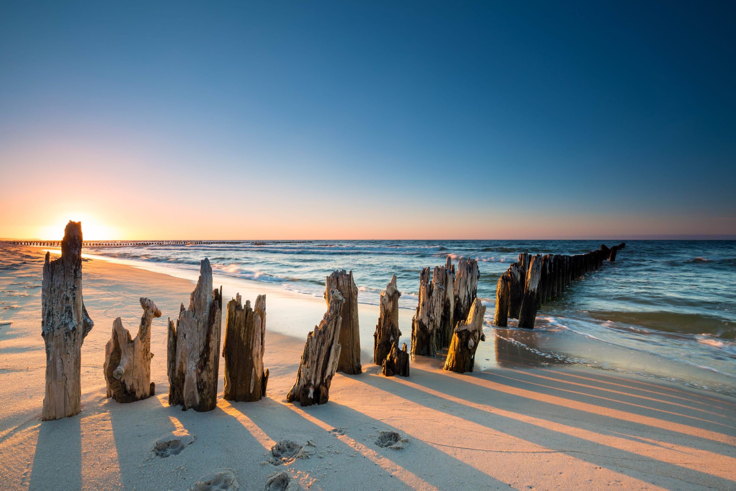 Sonnenuntergang am Strand mit Holzpfählen im Sand und ruhiger Brandung