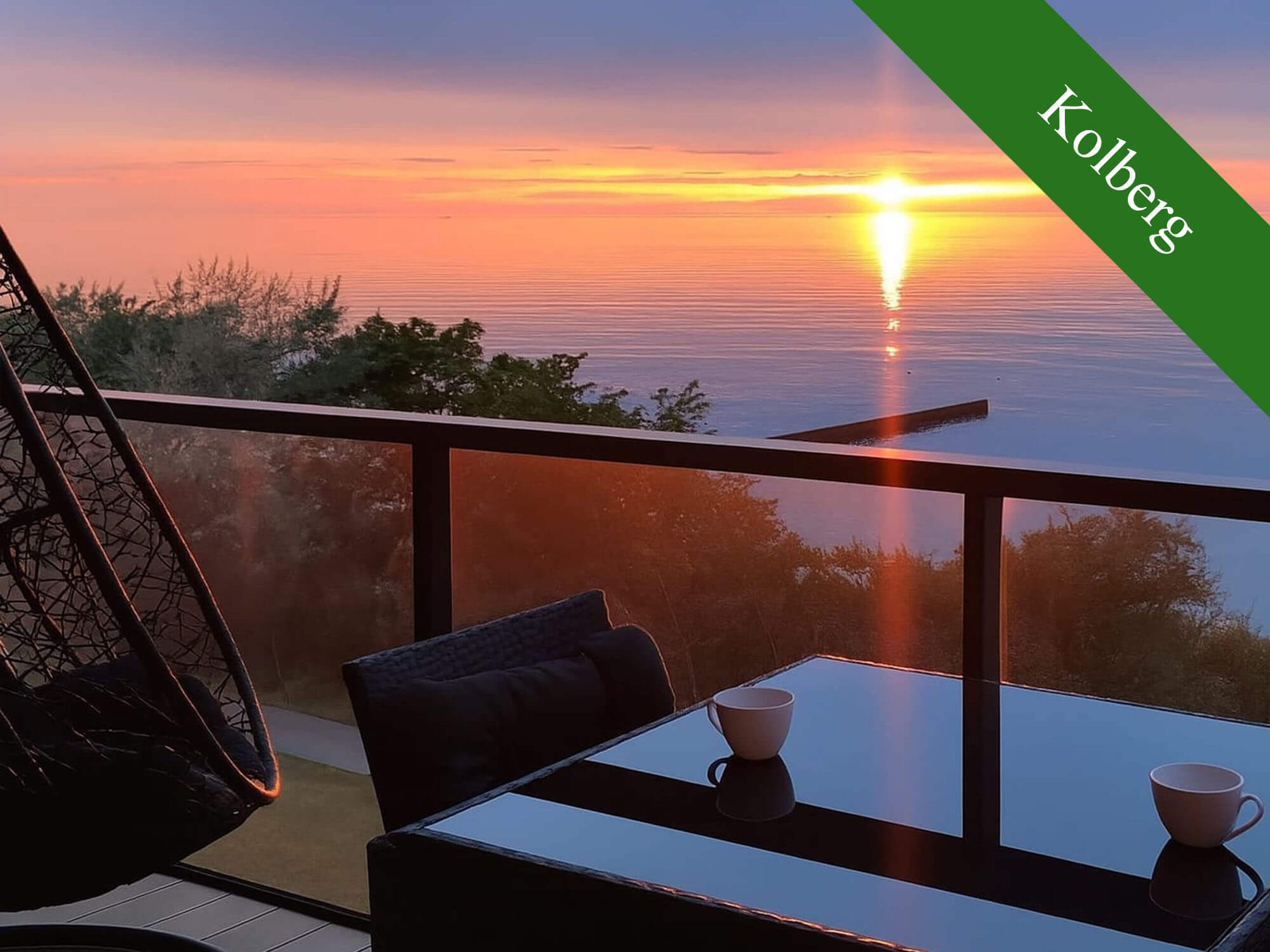 Sonnenuntergang über dem Wasser, gesehen von einem Balkon mit Tisch, Tassen und Hängesessel